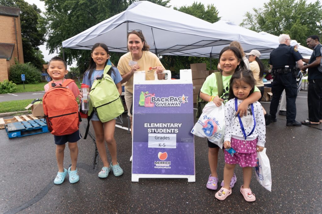 Children and a Merrick staff member at a backpack giveaway