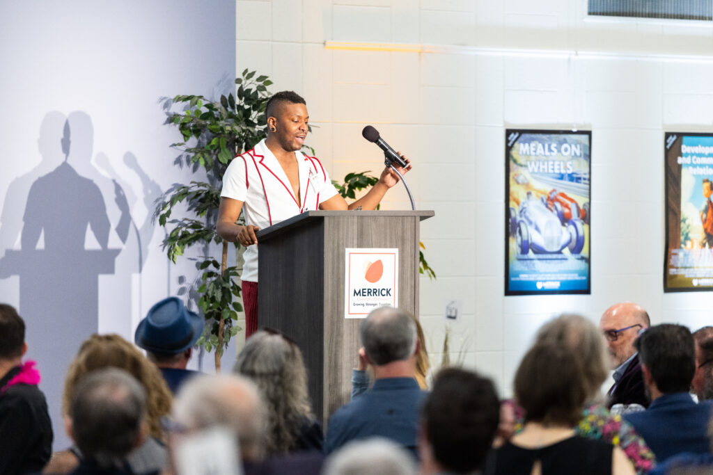 Speaker at a Merrick podium beside a Meals on Wheels display